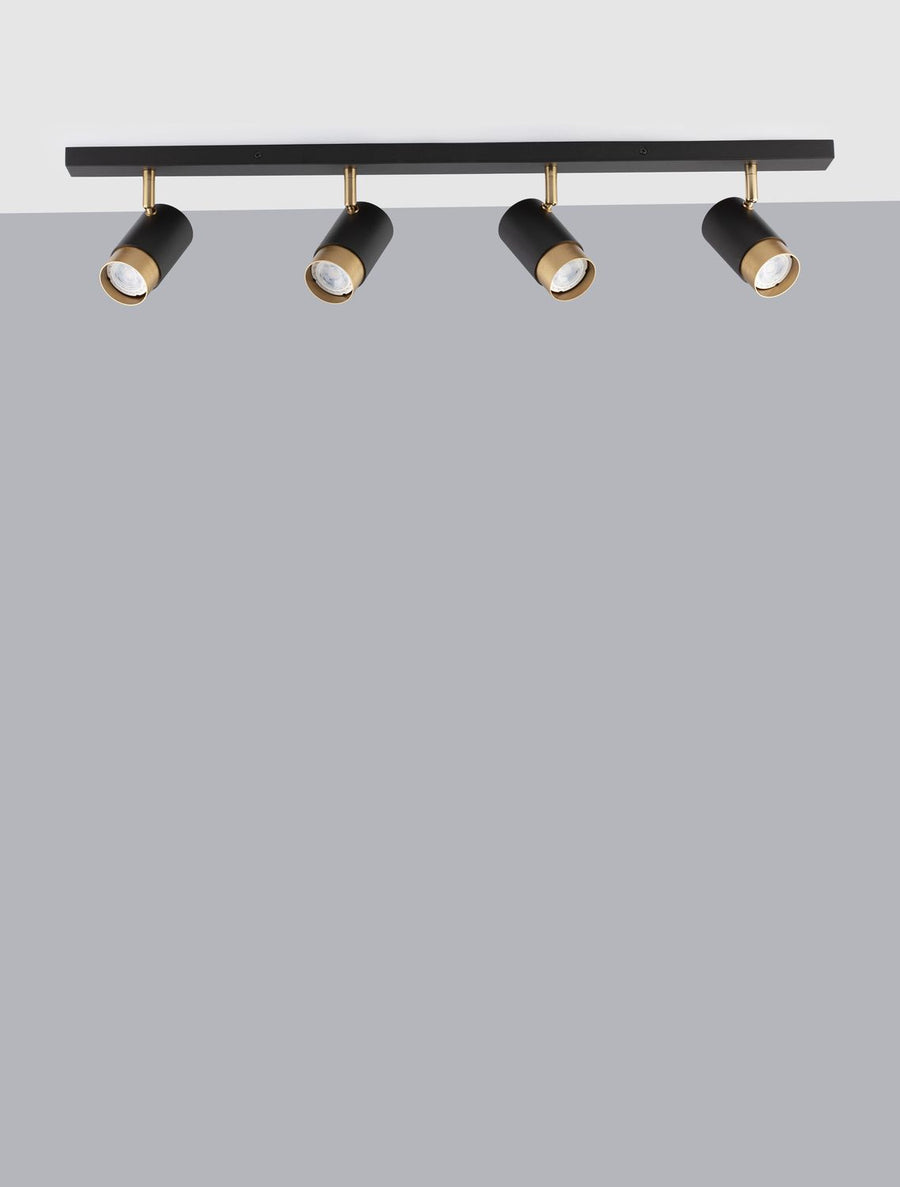 Vue de face sur fond gris du luminaire noir à quatre spots dorés fixés sur rail.