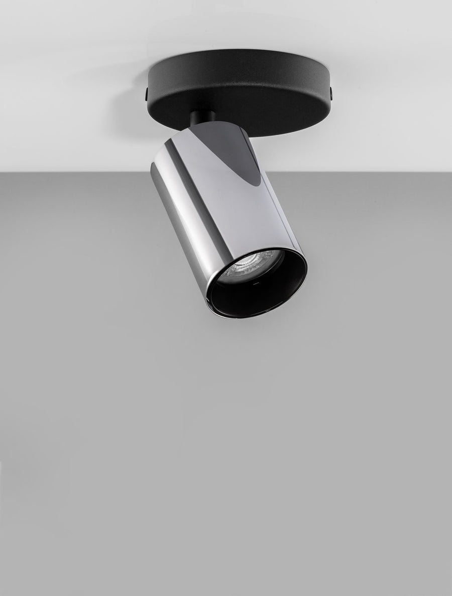 Luminaire installé au plafond, tête cylindrique inclinée éclairant un mur gris