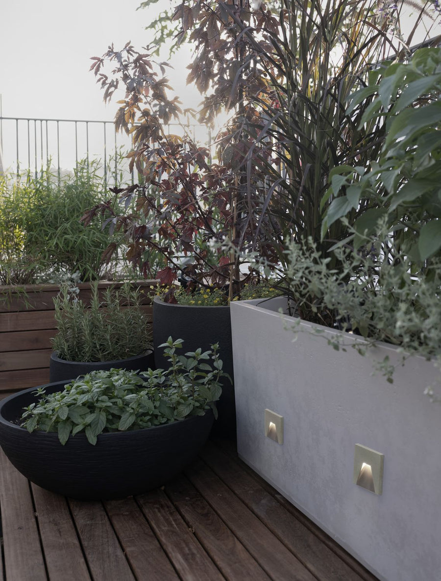 Deux appliques allumées sur une jardinière en béton, terrasse en bois plantée
