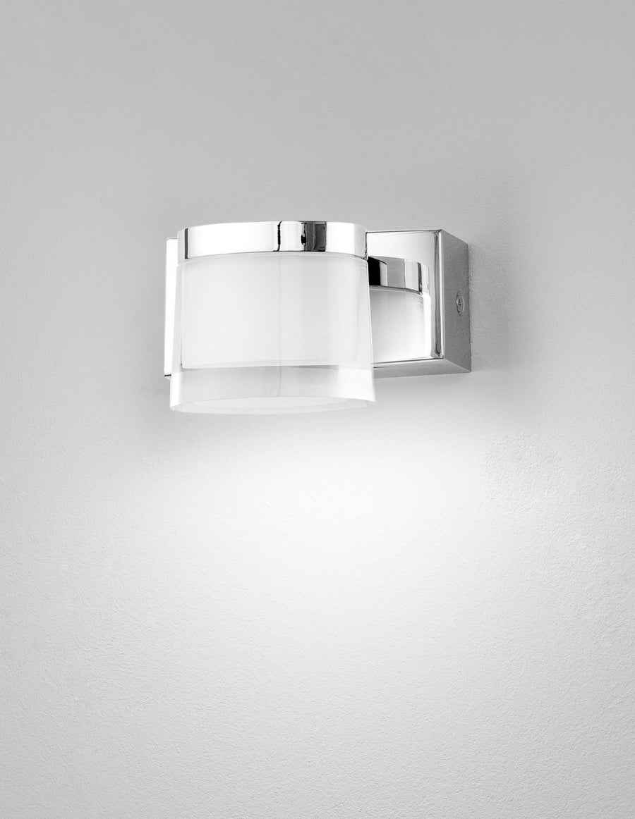 Applique murale chromée allumée sur mur blanc, halo lumineux diffus vers le bas