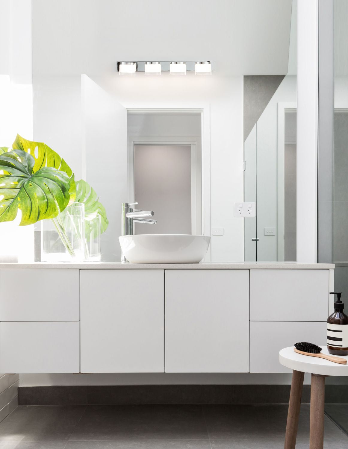 Applique chromée à quatre lumières installée au-dessus d'un miroir de salle de bain blanche