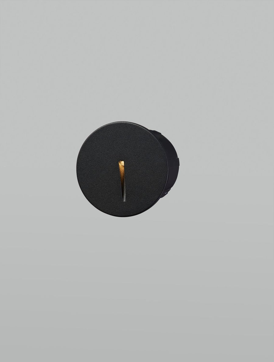 Applique noire allumée, la fente verticale diffuse une lumière chaude dorée.