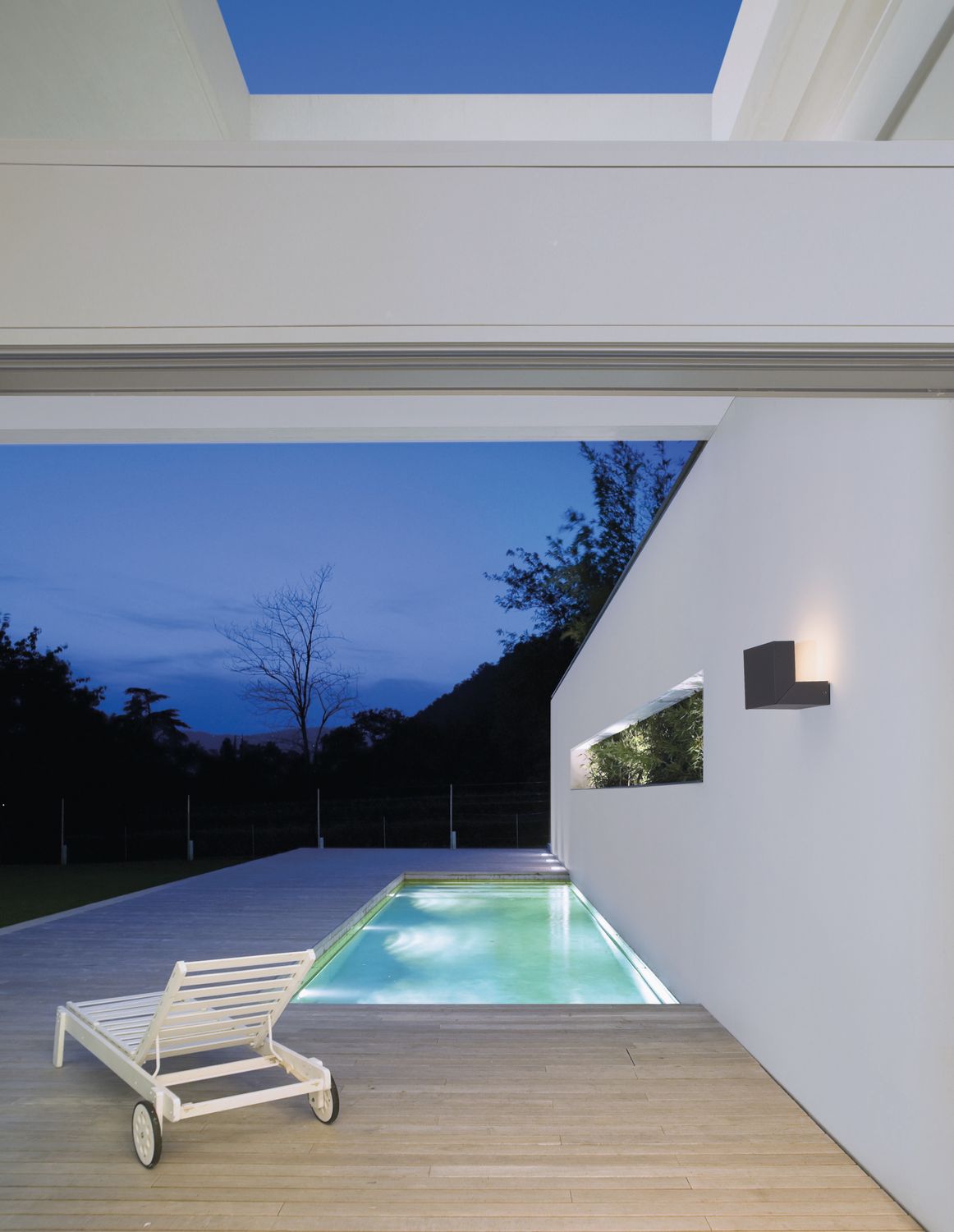 Applique anthracite éclairée sur mur blanc près d'une piscine au crépuscule