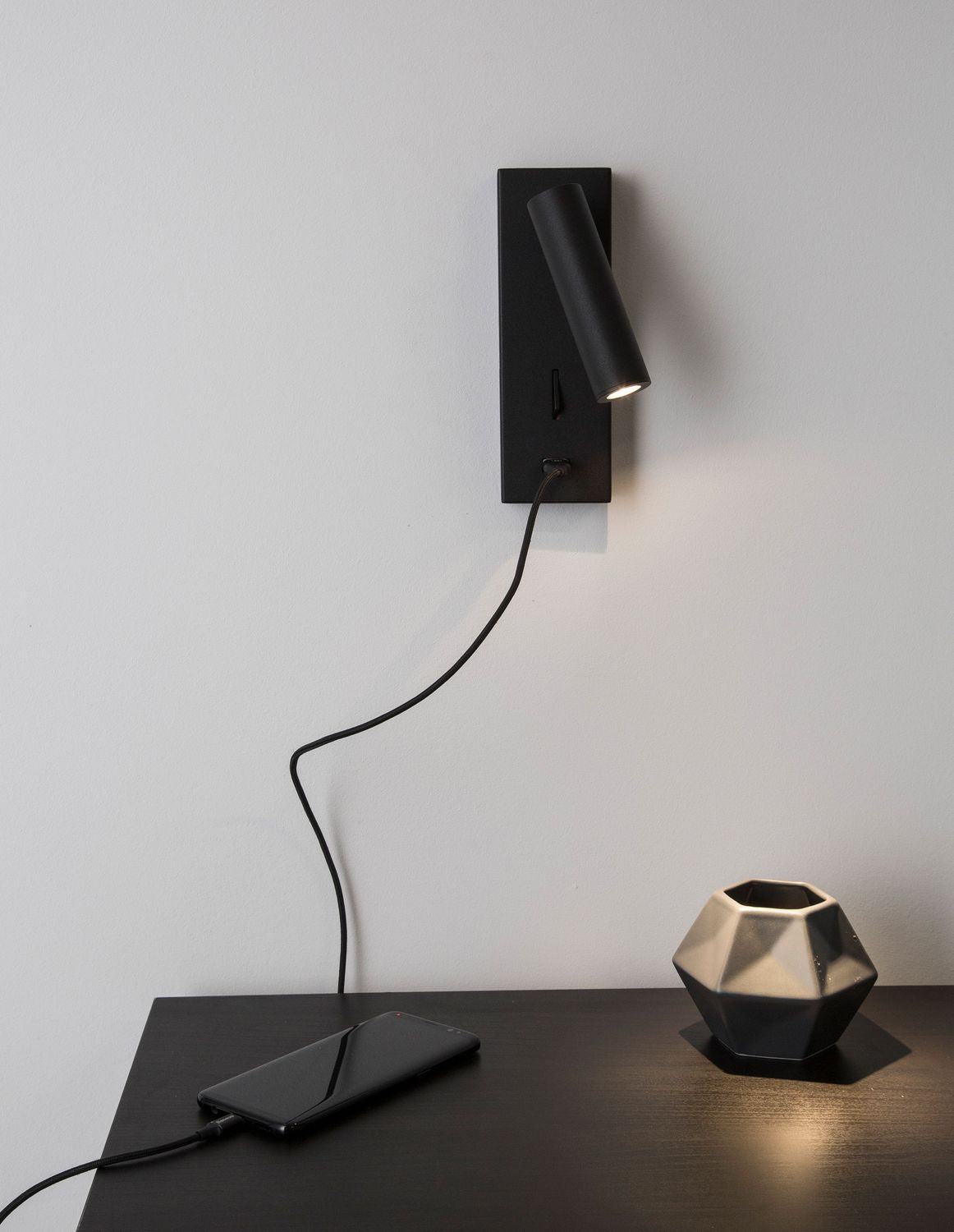 Applique murale noire fixée au-dessus d'une table, téléphone en charge, ambiance chambre