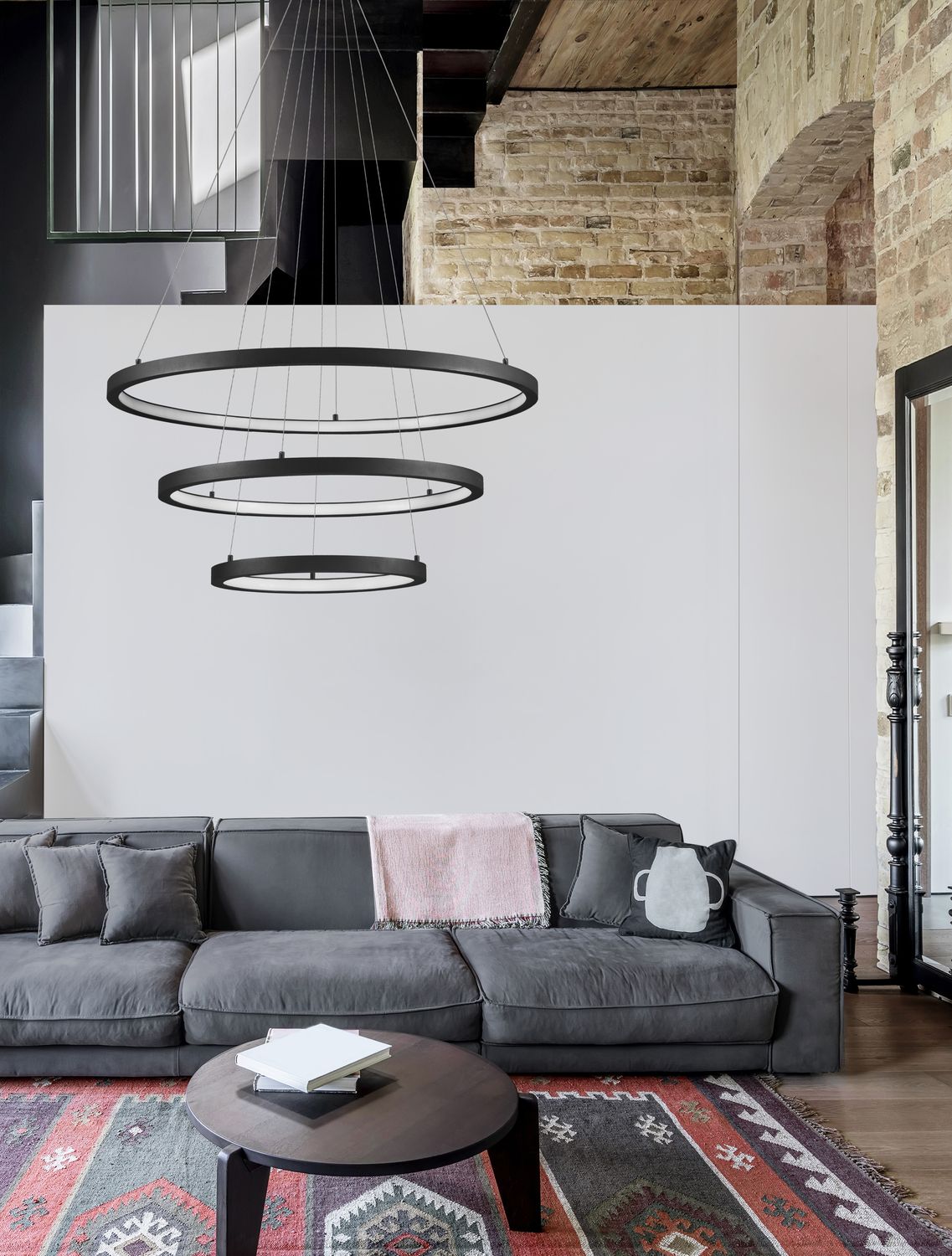Suspension à trois anneaux noirs surplombant un canapé gris dans un salon rustique.
