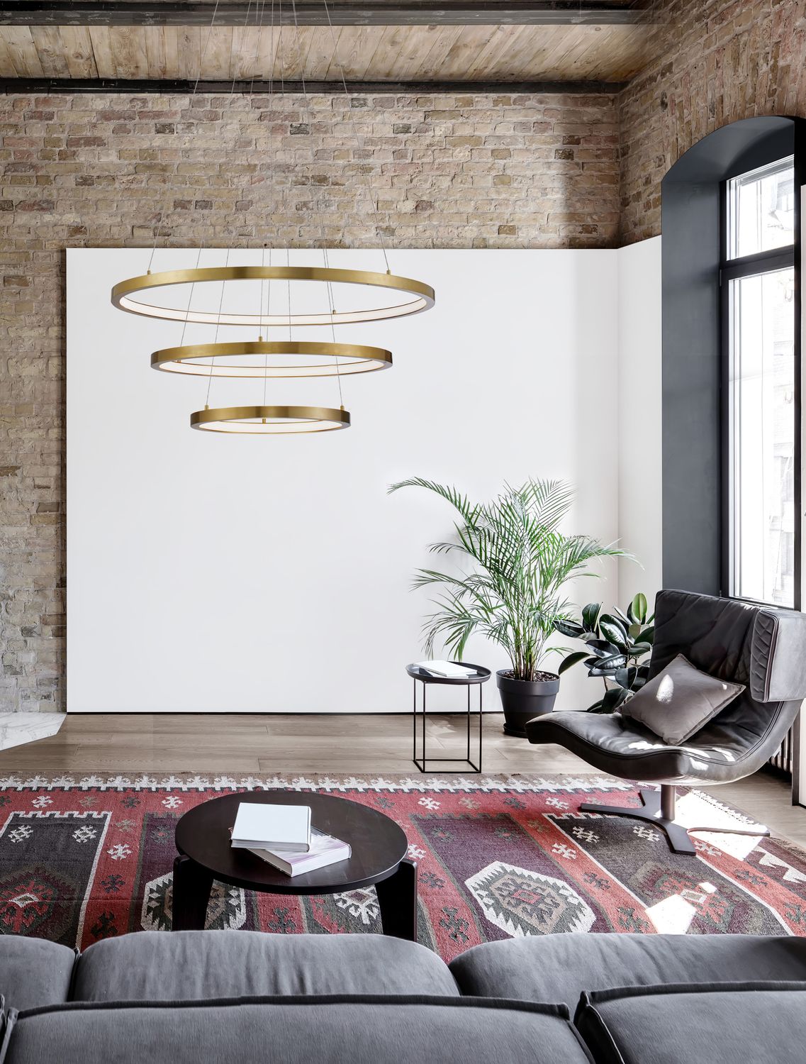 Suspension à trois anneaux dorés installée au-dessus d'un salon moderne dans un loft industriel.