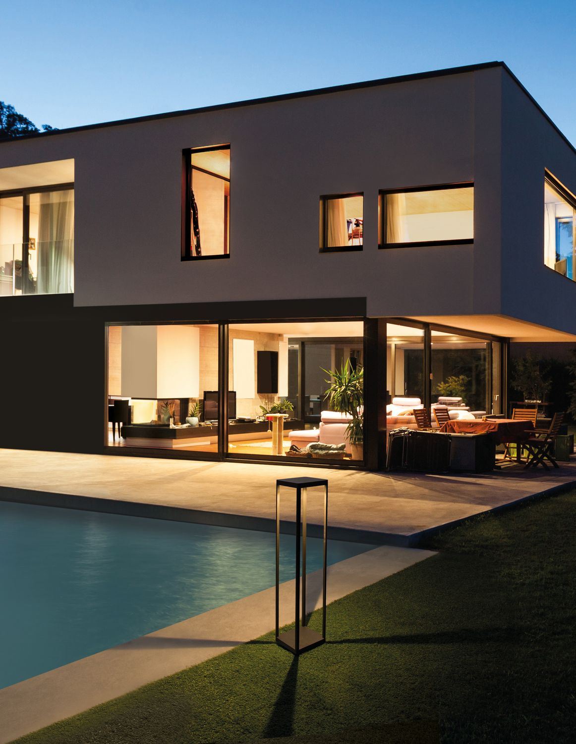 Borne lumineuse anthracite allumée sur pelouse au bord d'une piscine, maison moderne en fond