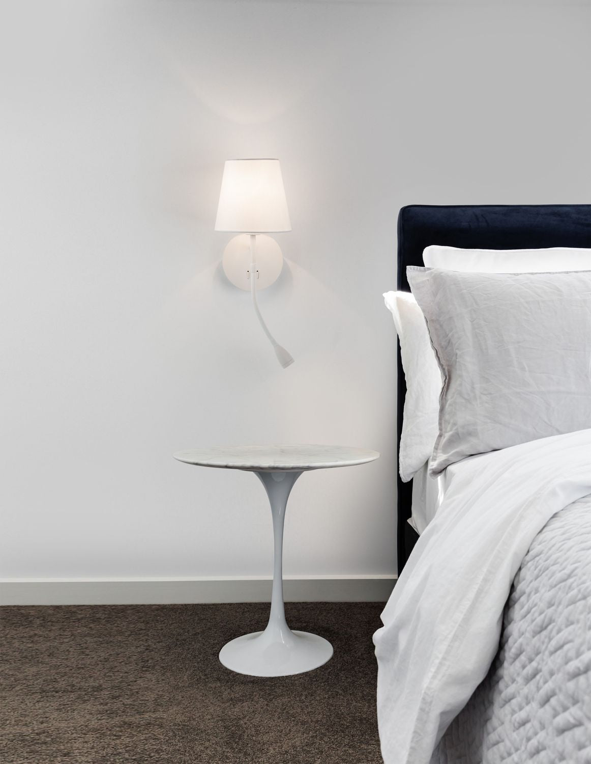Applique murale blanche allumée fixée au-dessus d'une table d'appoint, dans une chambre.