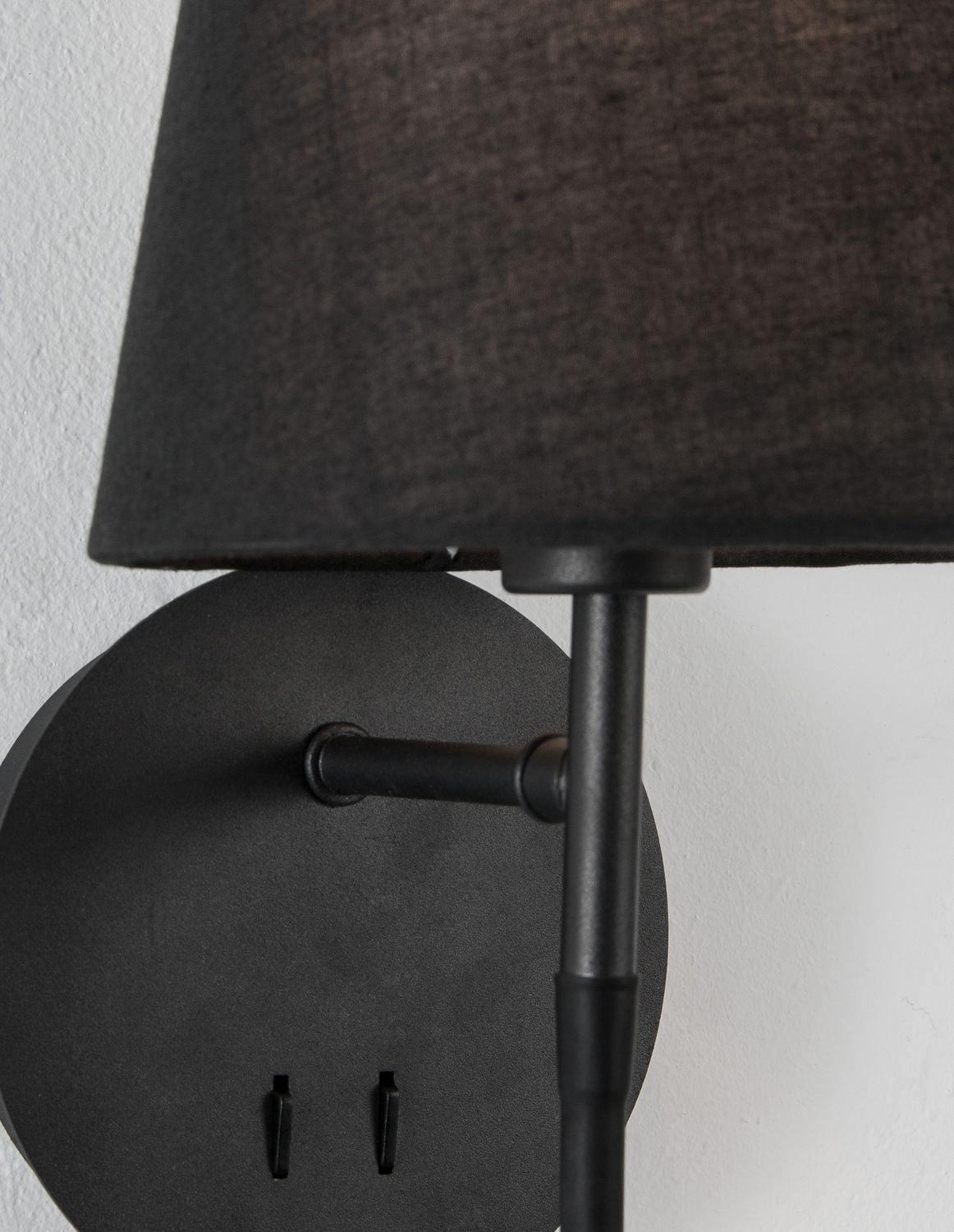 Détail du socle rond, du bras métallique et de l'abat-jour en tissu noir.