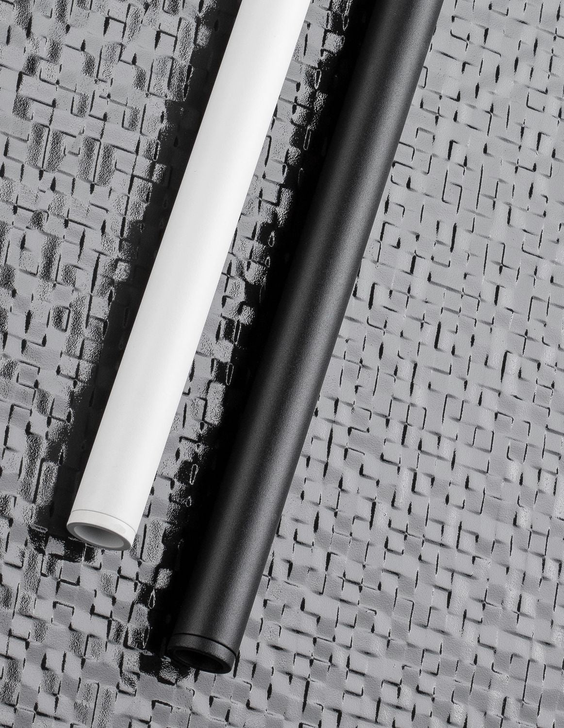 Détail de finition des tubes noir et blanc posés sur surface texturée.