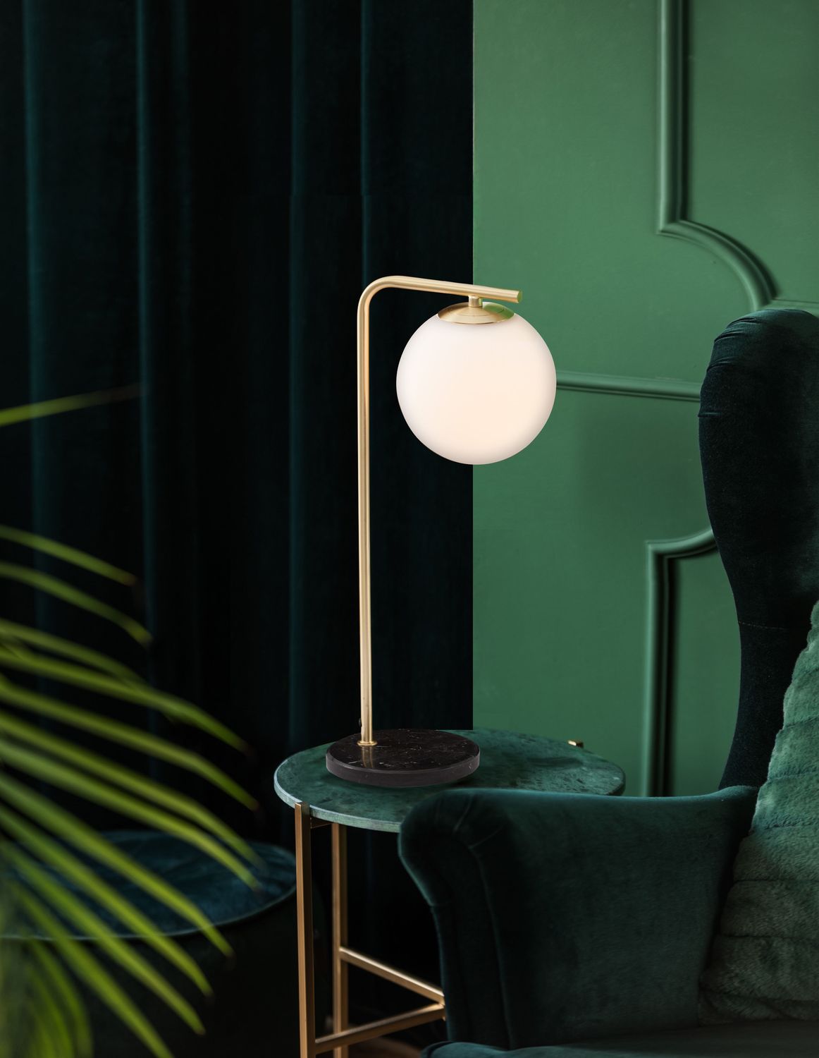Lampe à poser dorée avec globe en verre blanc posée sur une table d'appoint verte.