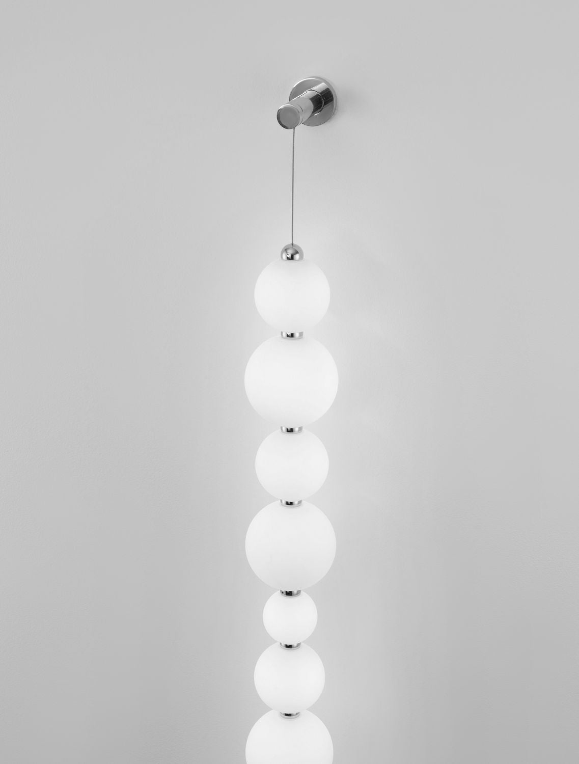 Applique murale chromée avec boules de verre blanches alignées verticalement sur un mur gris.