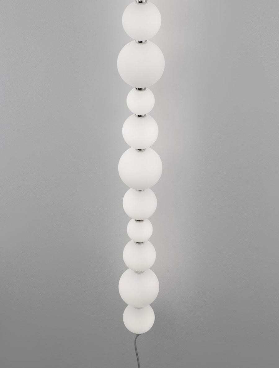 Détail rapproché des boules de verre blanches alternées et des jonctions chromées de l'applique.