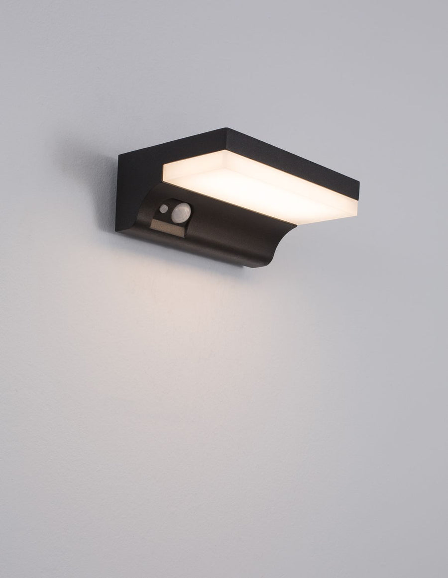 Applique allumée diffusant une lumière blanche sur le mur, capot anthracite ouvert.