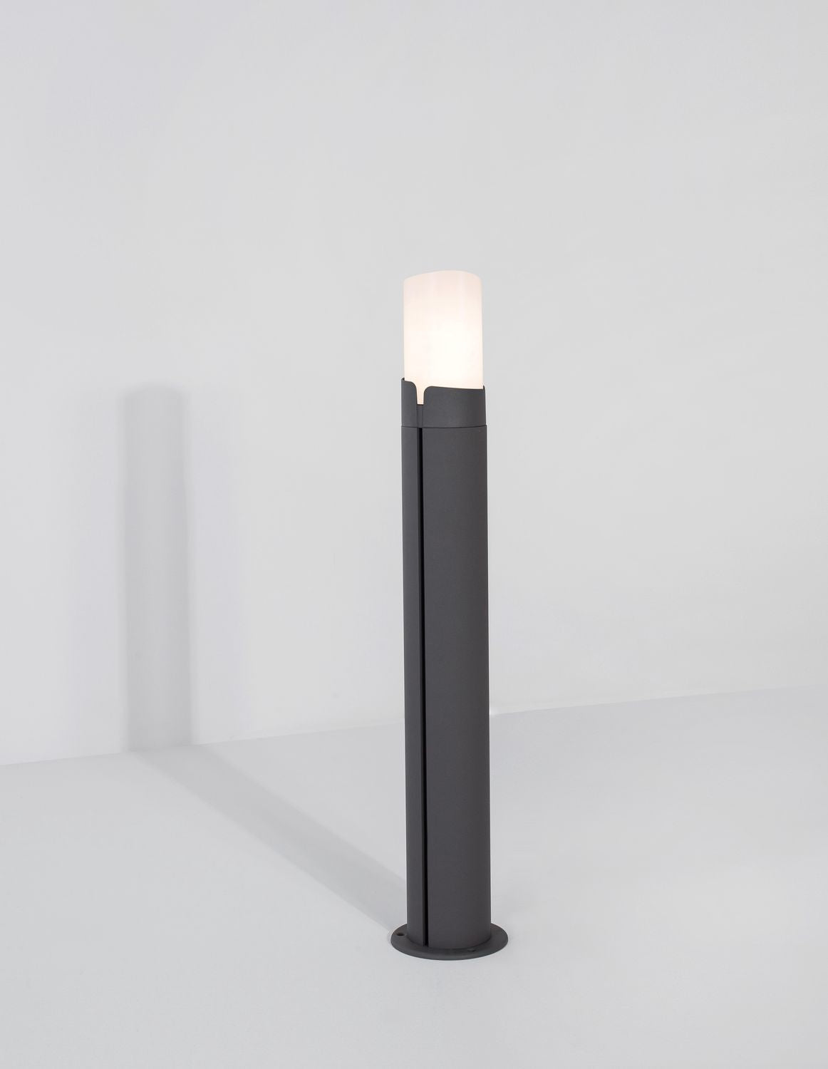 Borne grise allumée, son diffuseur blanc émet une lumière chaude, vue entière sur fond blanc.