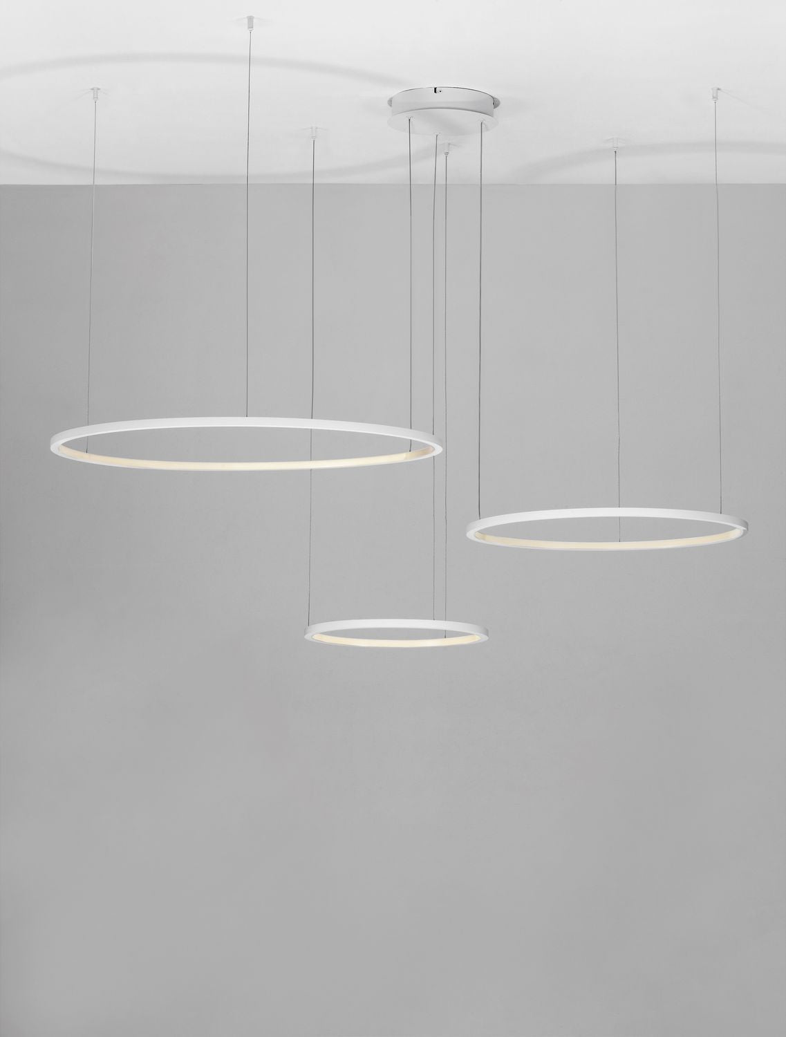Mise en ambiance de la suspension allumée, anneaux blancs diffusant une lumière chaude sur fond gris.
