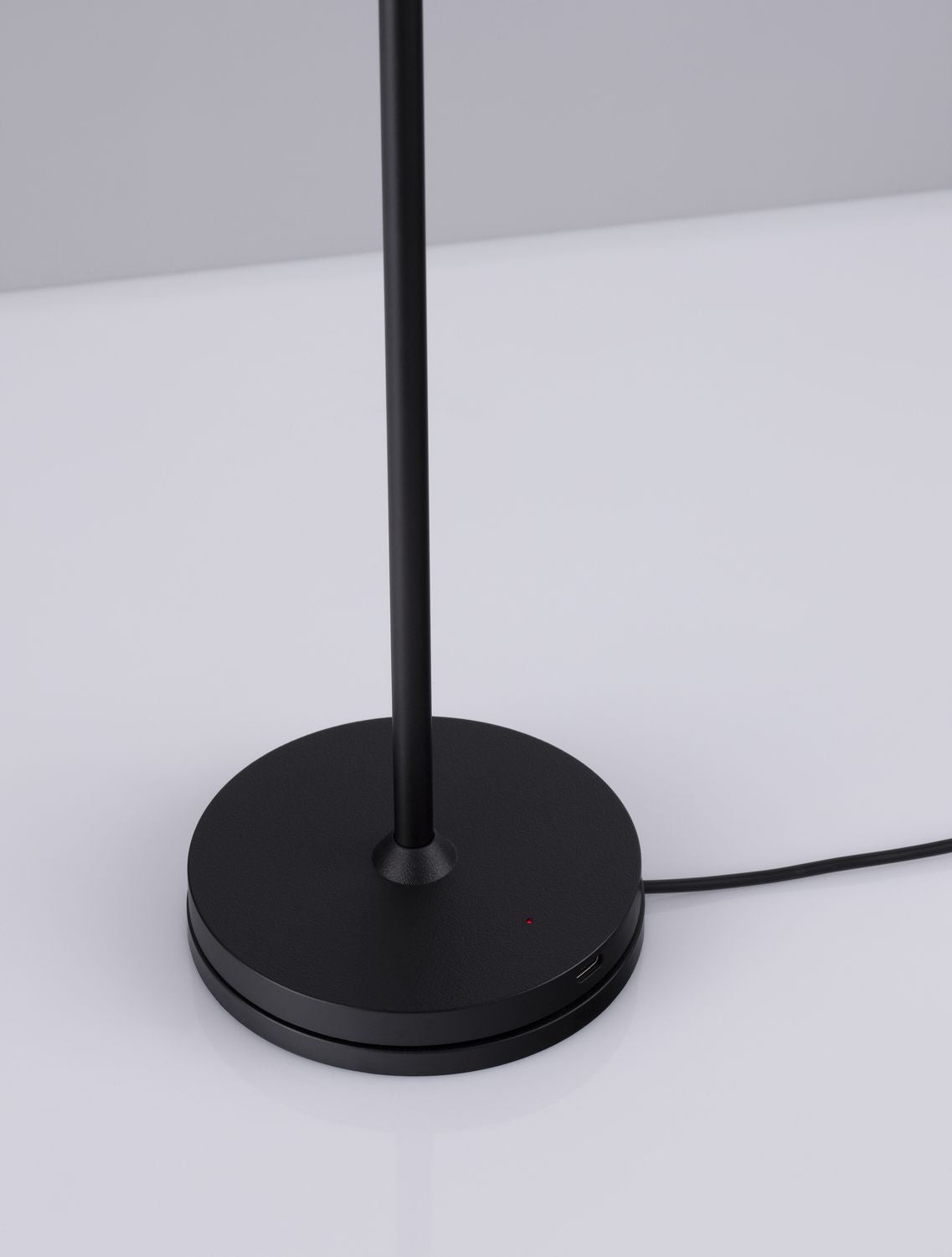 Détail de la base ronde noire avec câble d'alimentation, port USB et témoin lumineux rouge.