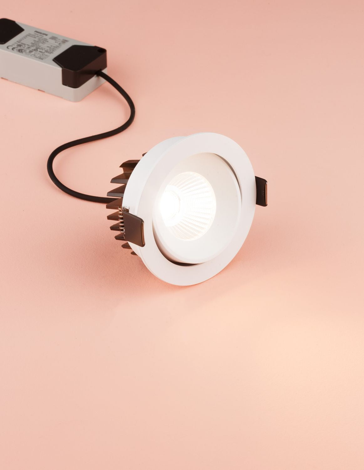 Vue d'ensemble du projecteur encastrable blanc avec son driver et son câble sur fond rose.