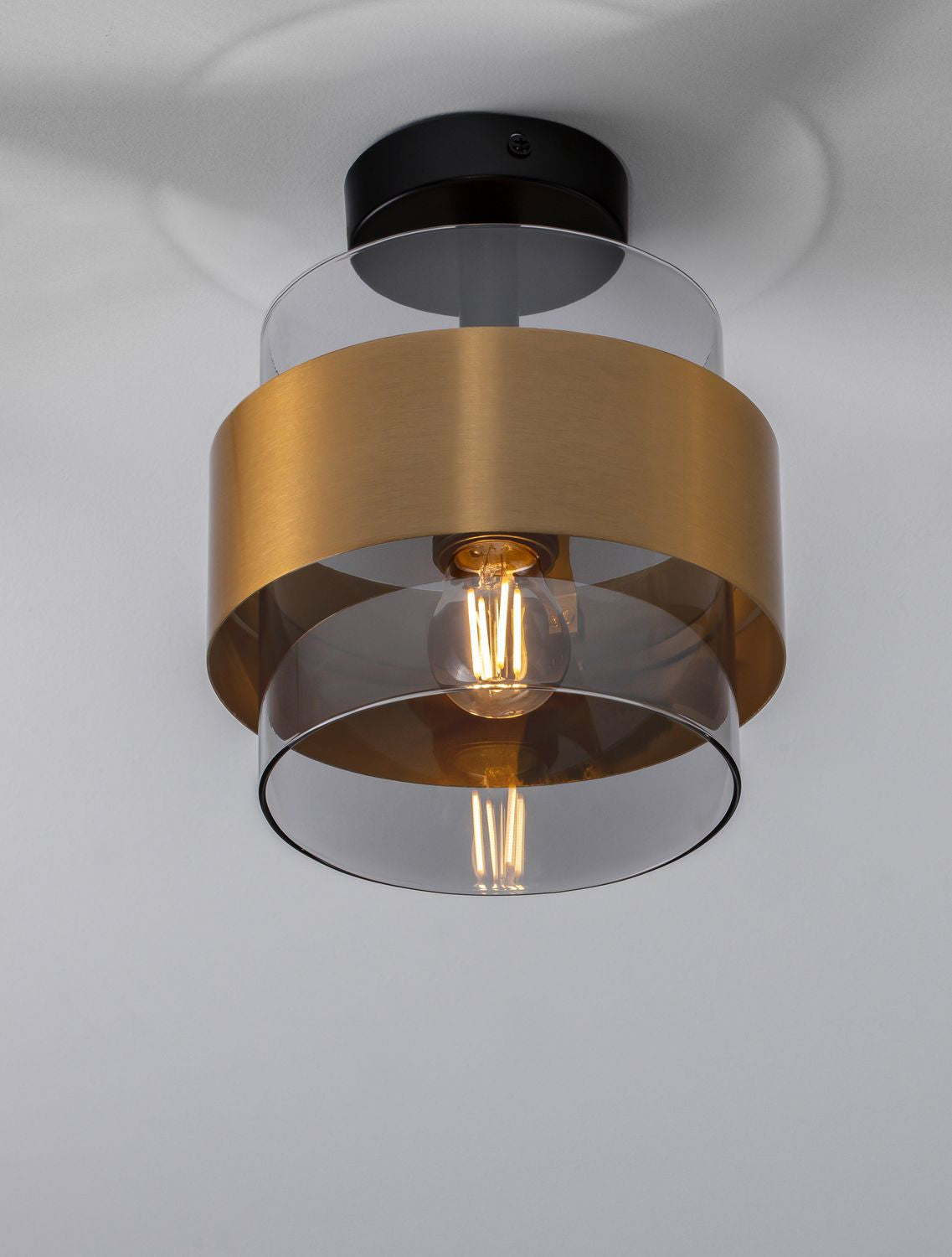 Plafonnier doré et verre fumé vu de face, fixé sous un plafond blanc