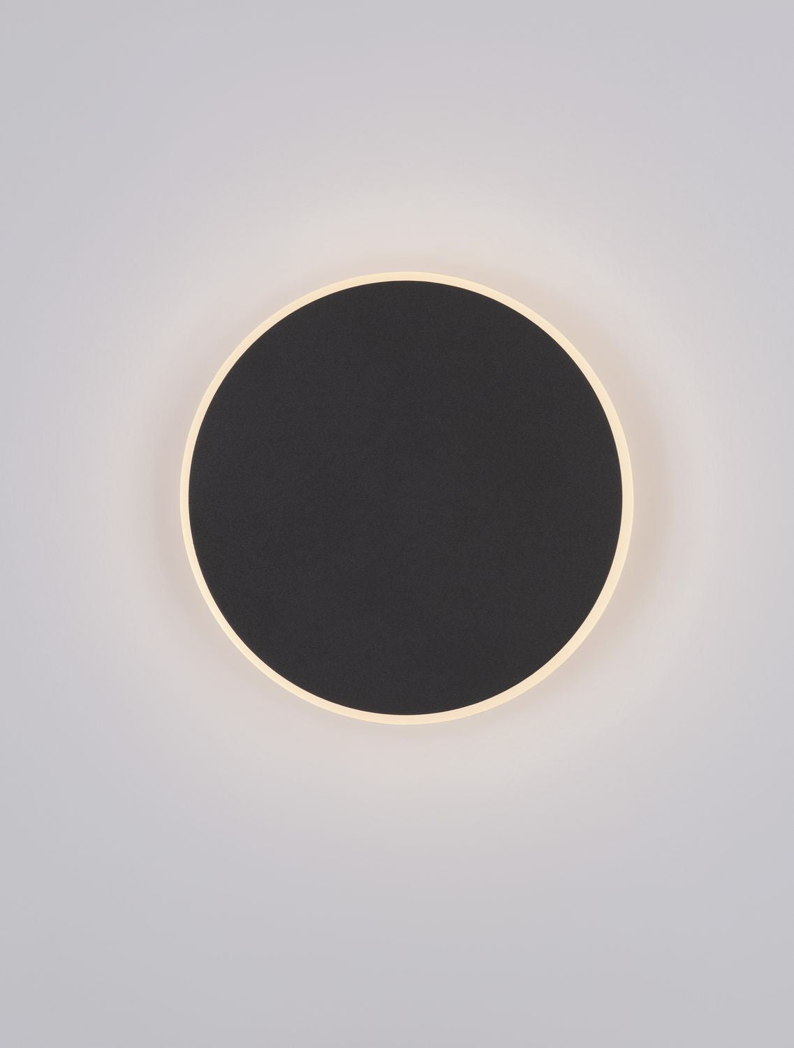 Applique murale ronde noire allumée, halo de lumière chaude sur fond gris clair
