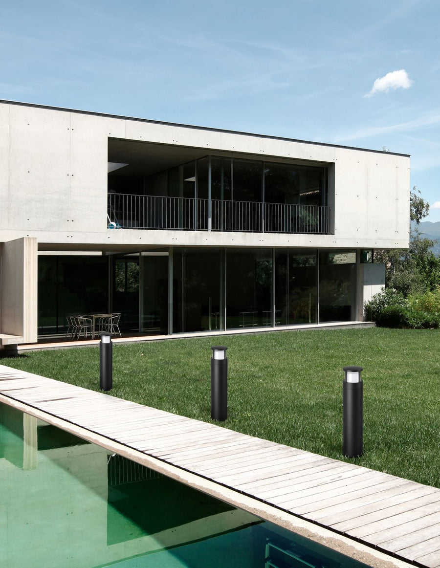 Trois bornes noires alignées sur la pelouse près d'une piscine, maison en béton