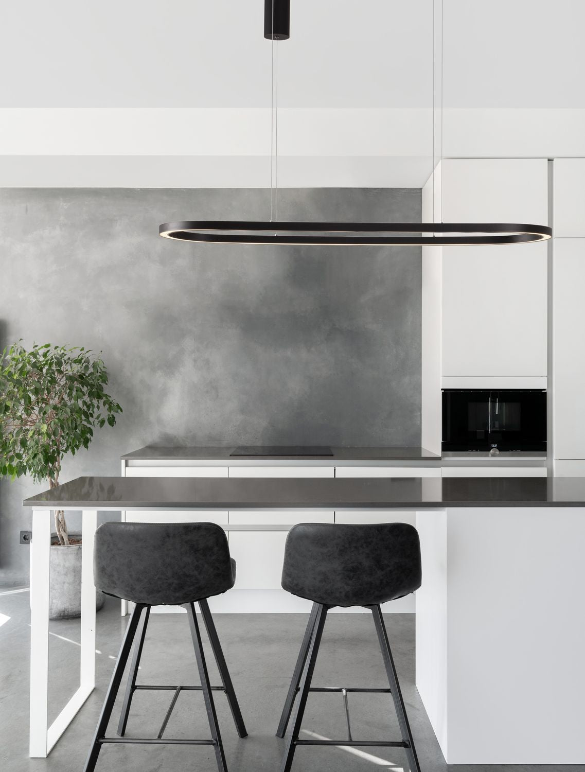 Suspension noire ovale au-dessus d'un îlot de cuisine, deux tabourets et mur gris