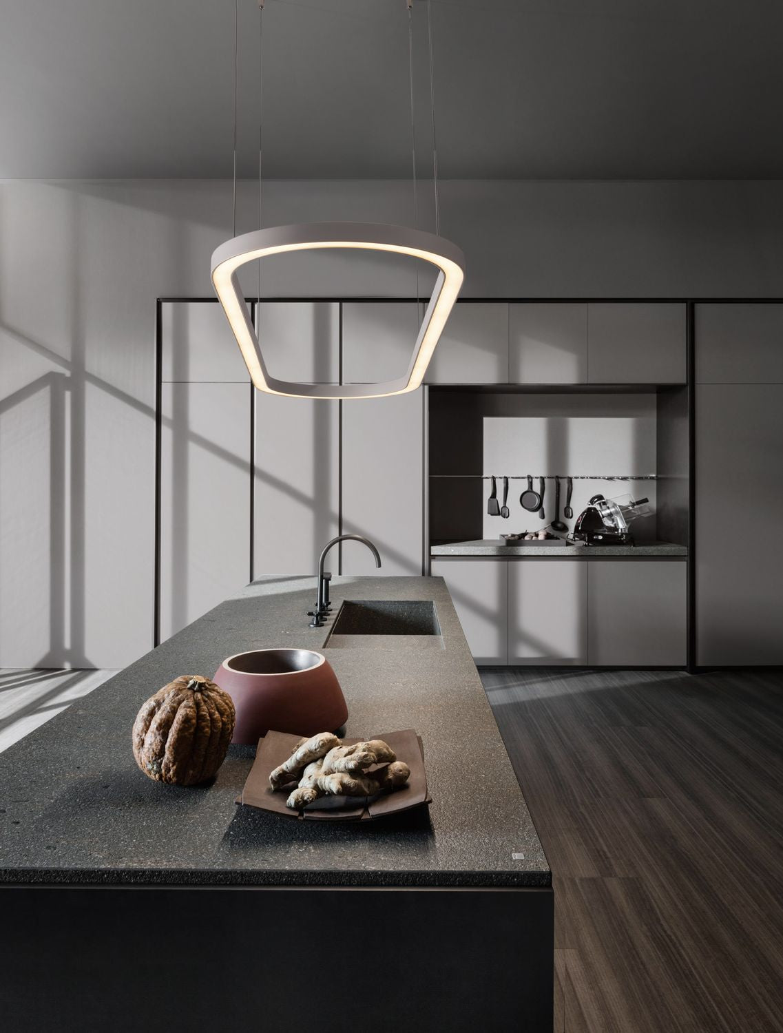 Suspension lumineuse allumée au-dessus d'un îlot de cuisine moderne, ambiance sombre et épurée.