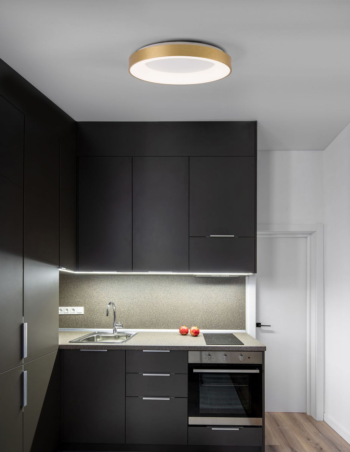 Plafonnier doré circulaire allumé au plafond d'une cuisine sombre moderne