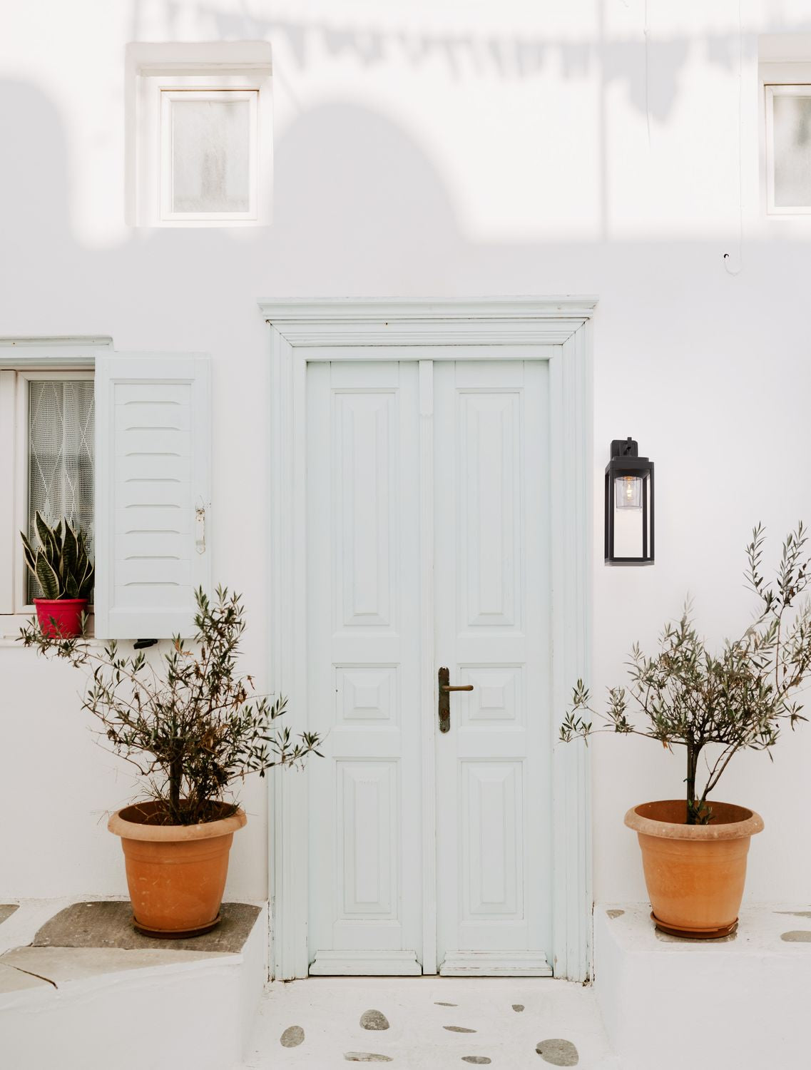 Applique noire installée sur un mur blanc, près d'une porte et de plantes en pot