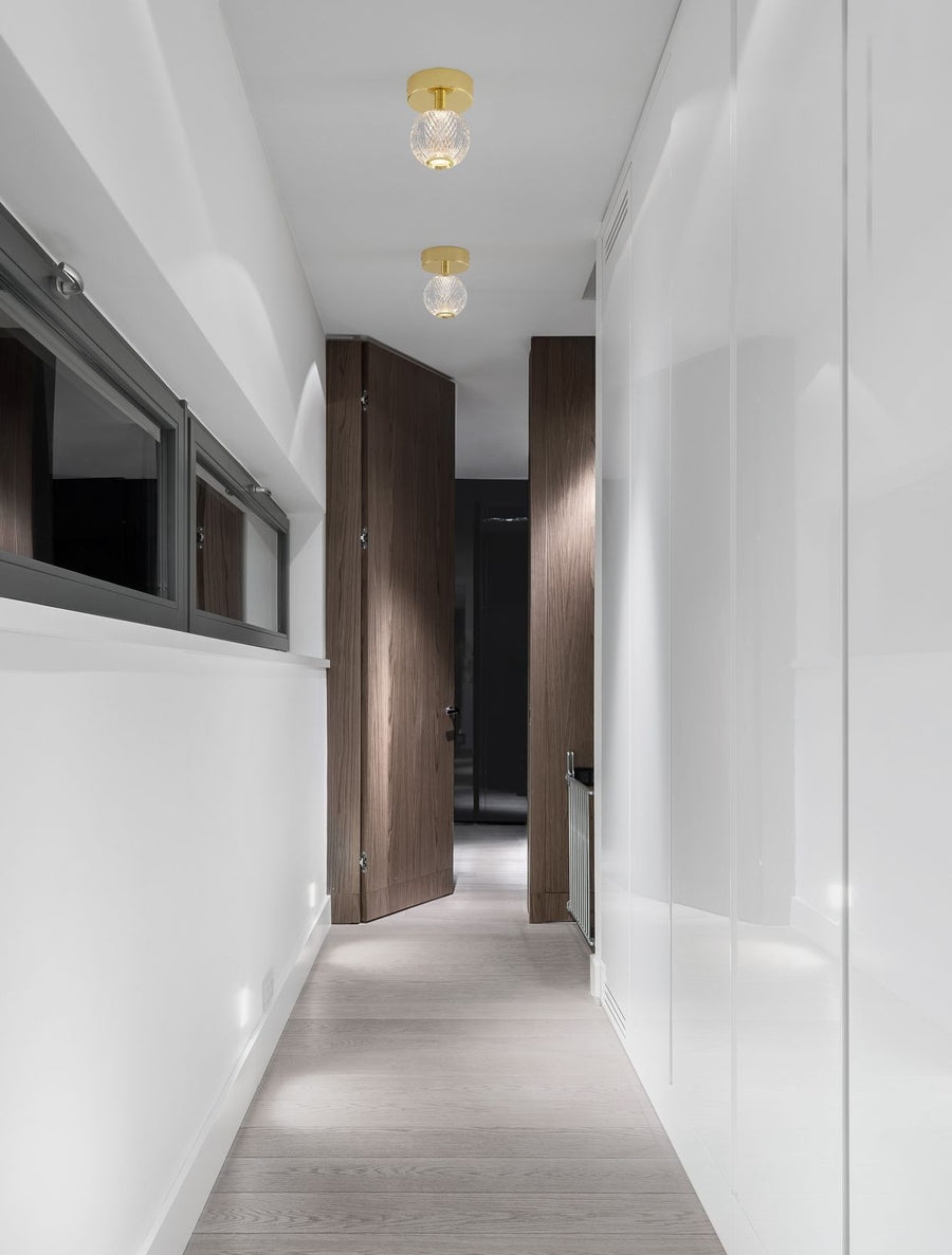 Couloir blanc avec deux plafonniers dorés allumés, portes en bois foncé et sol clair.