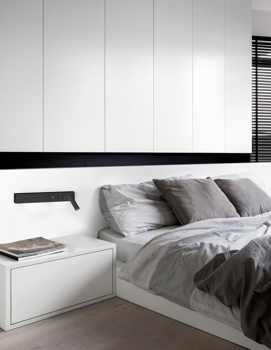 Applique noire fixée au mur au-dessus d'une table de chevet dans une chambre claire