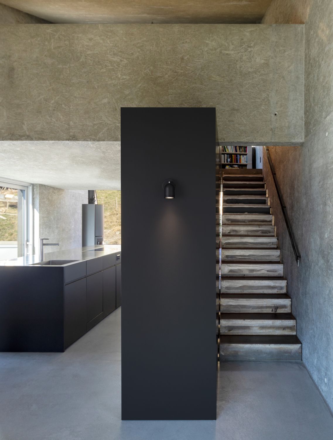 Vue d'ambiance dans un intérieur béton, spot noir fixé sur une cloison verticale sombre