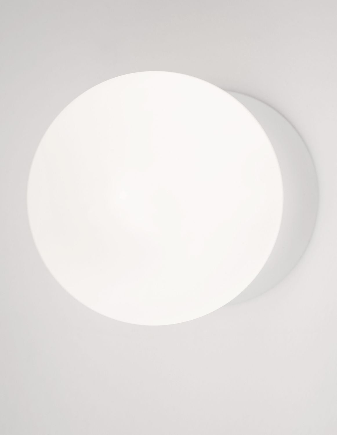 Globe lumineux blanc vu de face, halo doux sur le mur