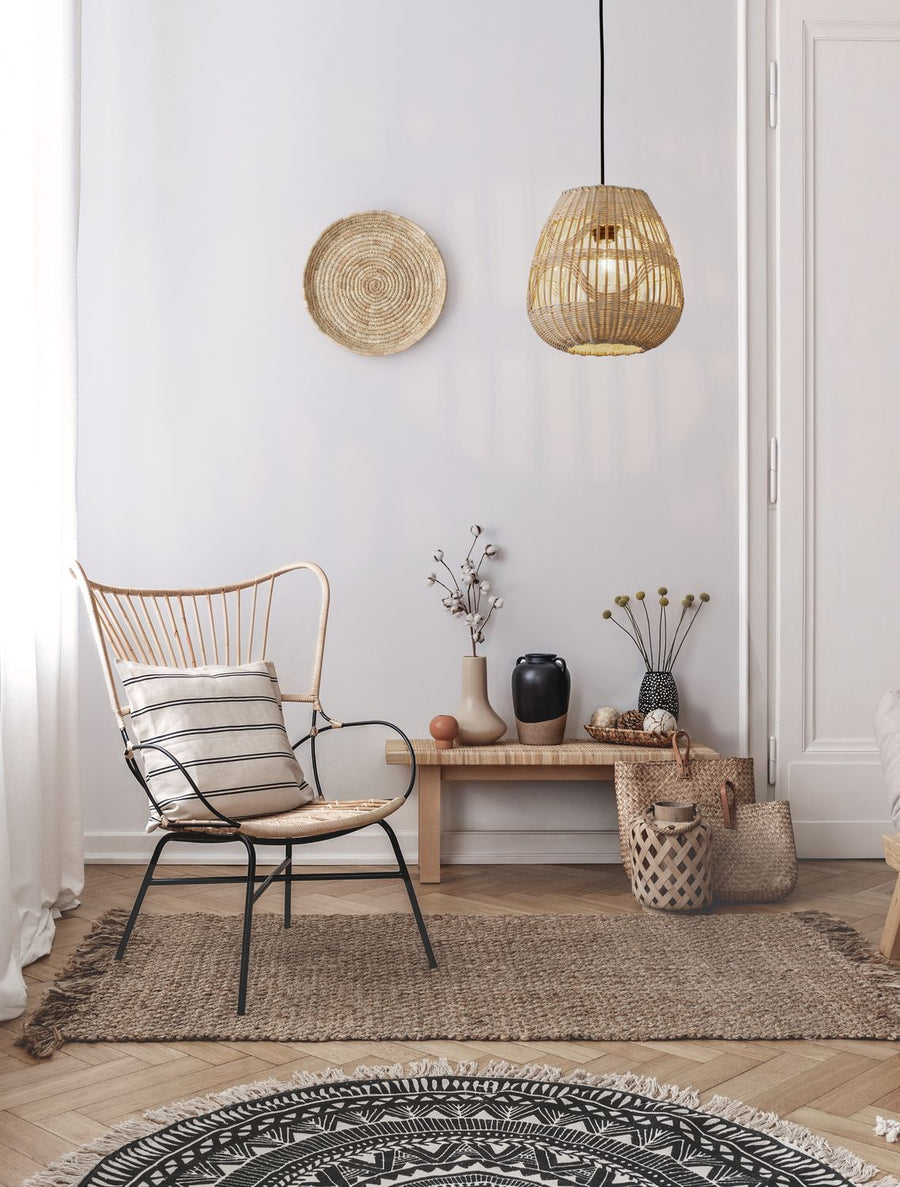 Suspension en rotin beige allumée dans un salon bohème, fauteuil et panier mural assortis.