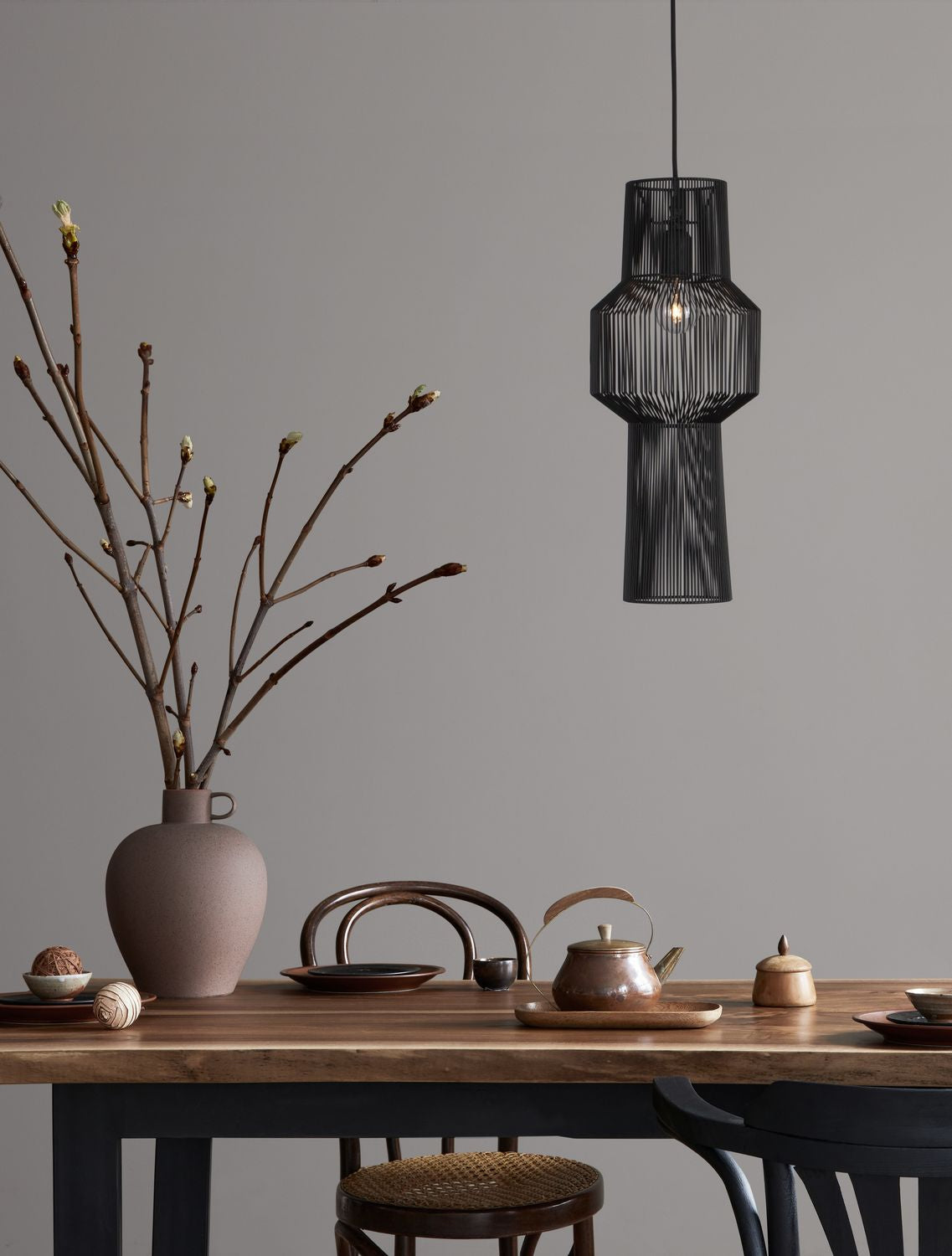 Suspension noire au-dessus d'une table en bois, vase et théière en ambiance