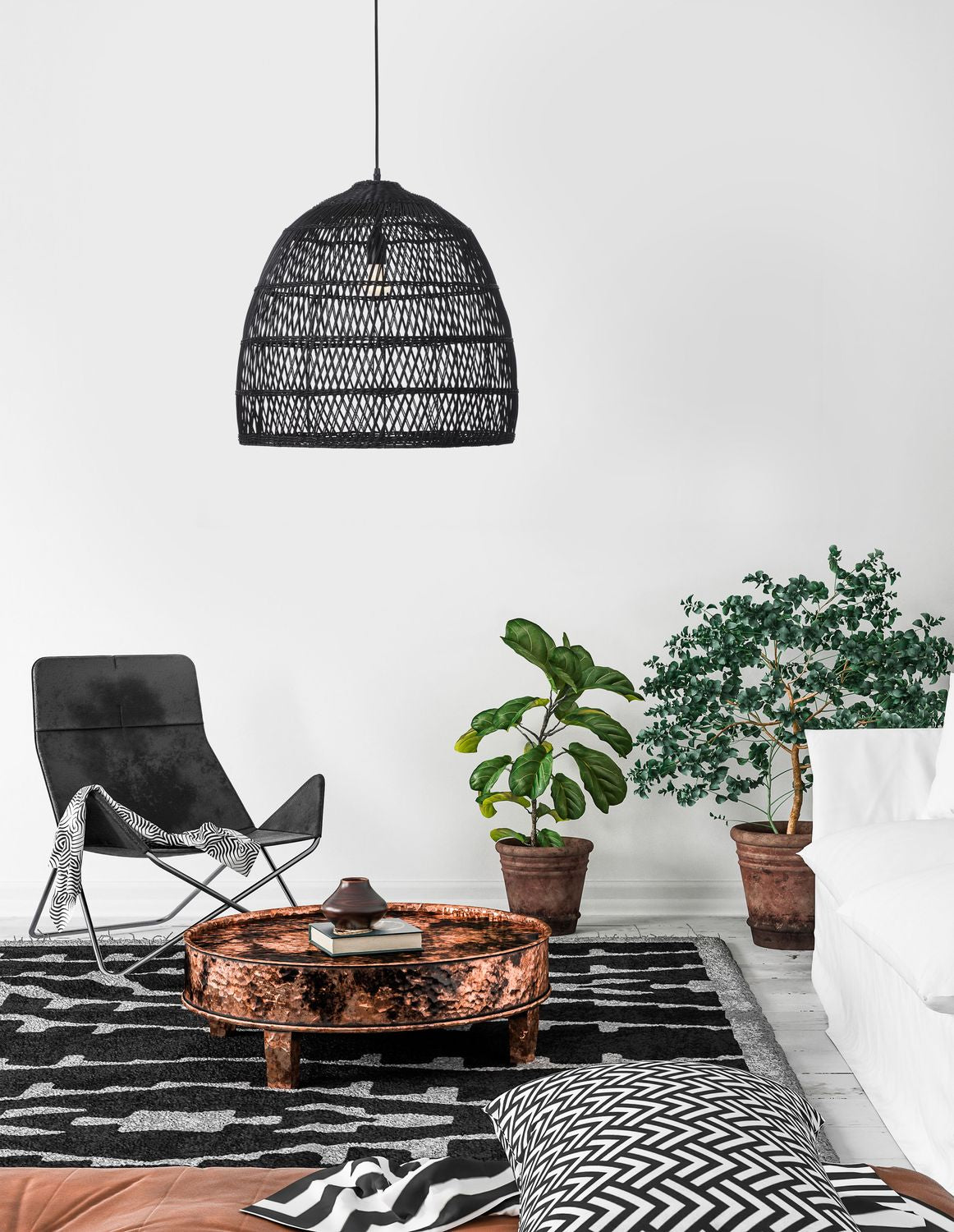 Suspension noire en rotin suspendue au-dessus d'un salon avec fauteuil et plantes.