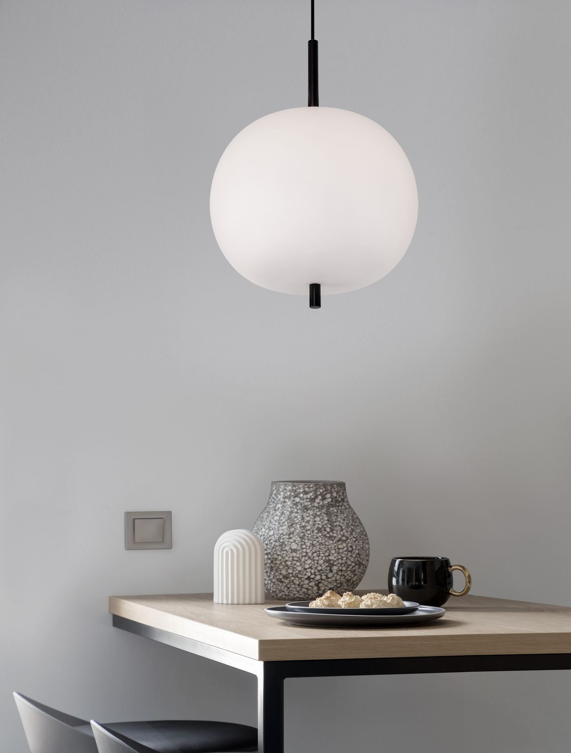 Suspension allumée au-dessus d'une table en bois dans un intérieur gris clair