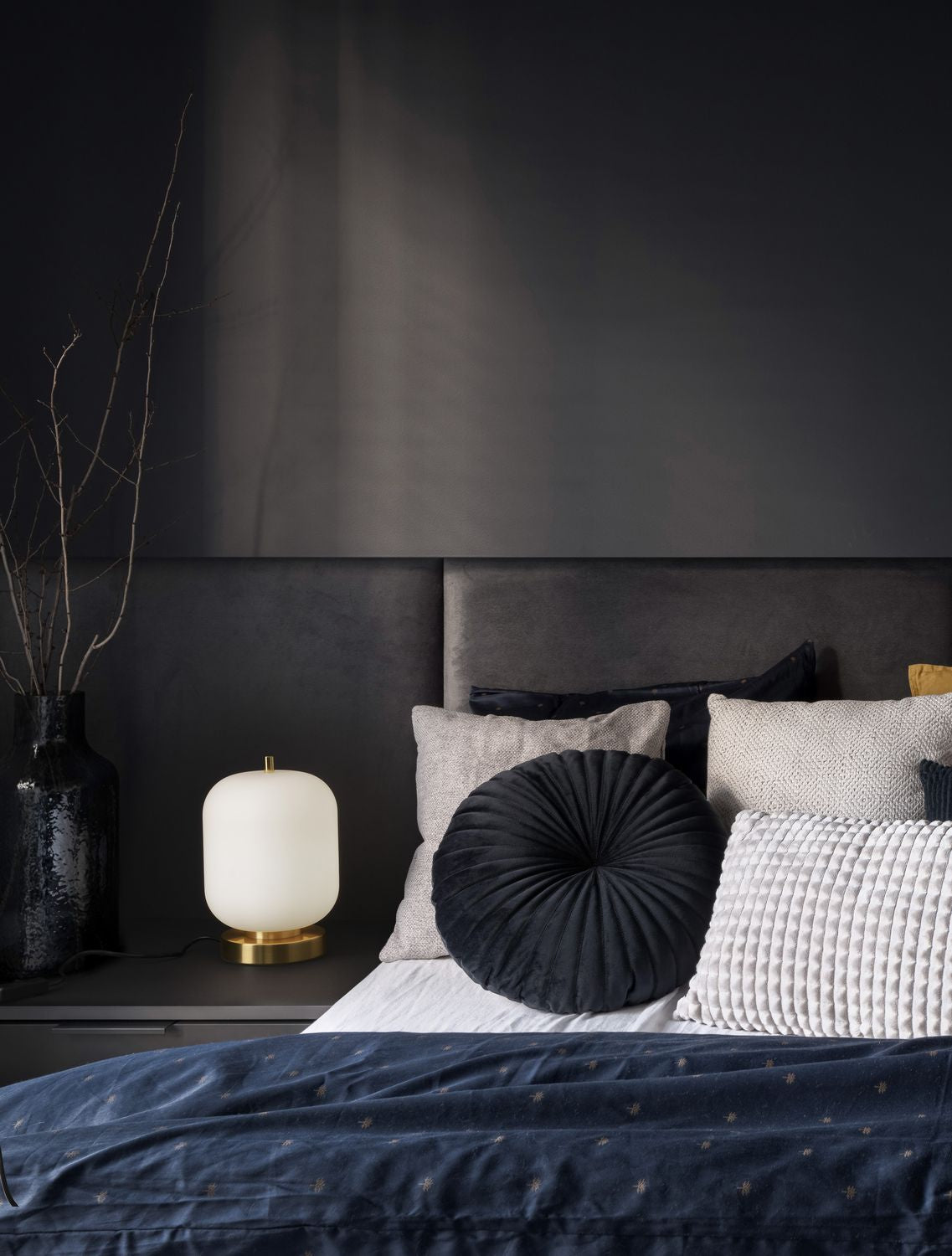 Lampe allumée posée sur une table de nuit dans une chambre sombre et feutrée