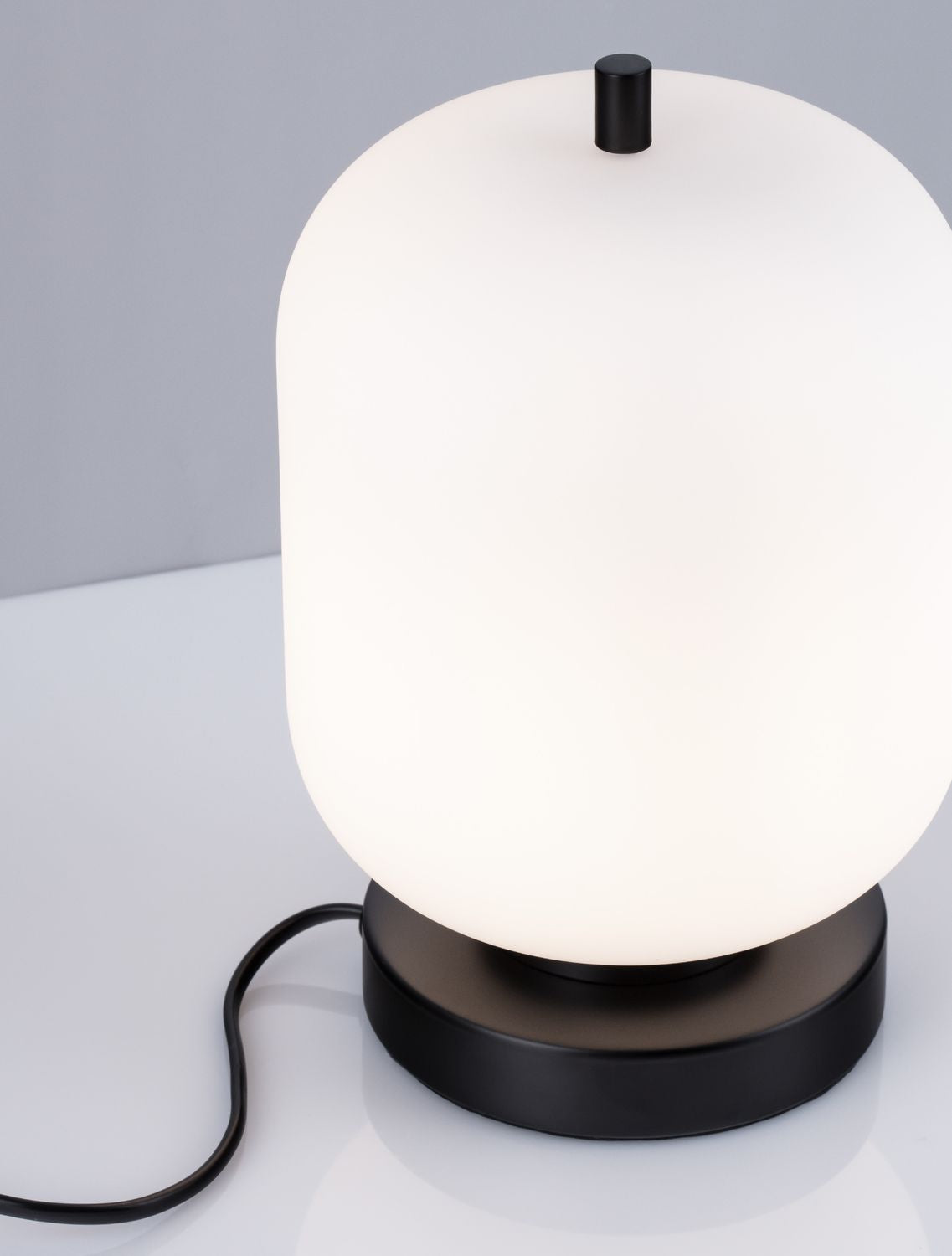 Gros plan du luminaire, abat-jour en verre opalin blanc et détail cylindrique noir.