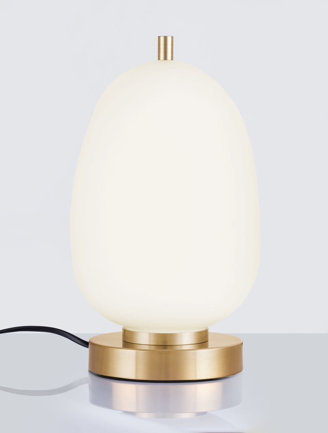 Gros plan de la base dorée et du câble, lampe allumée sur surface réfléchissante