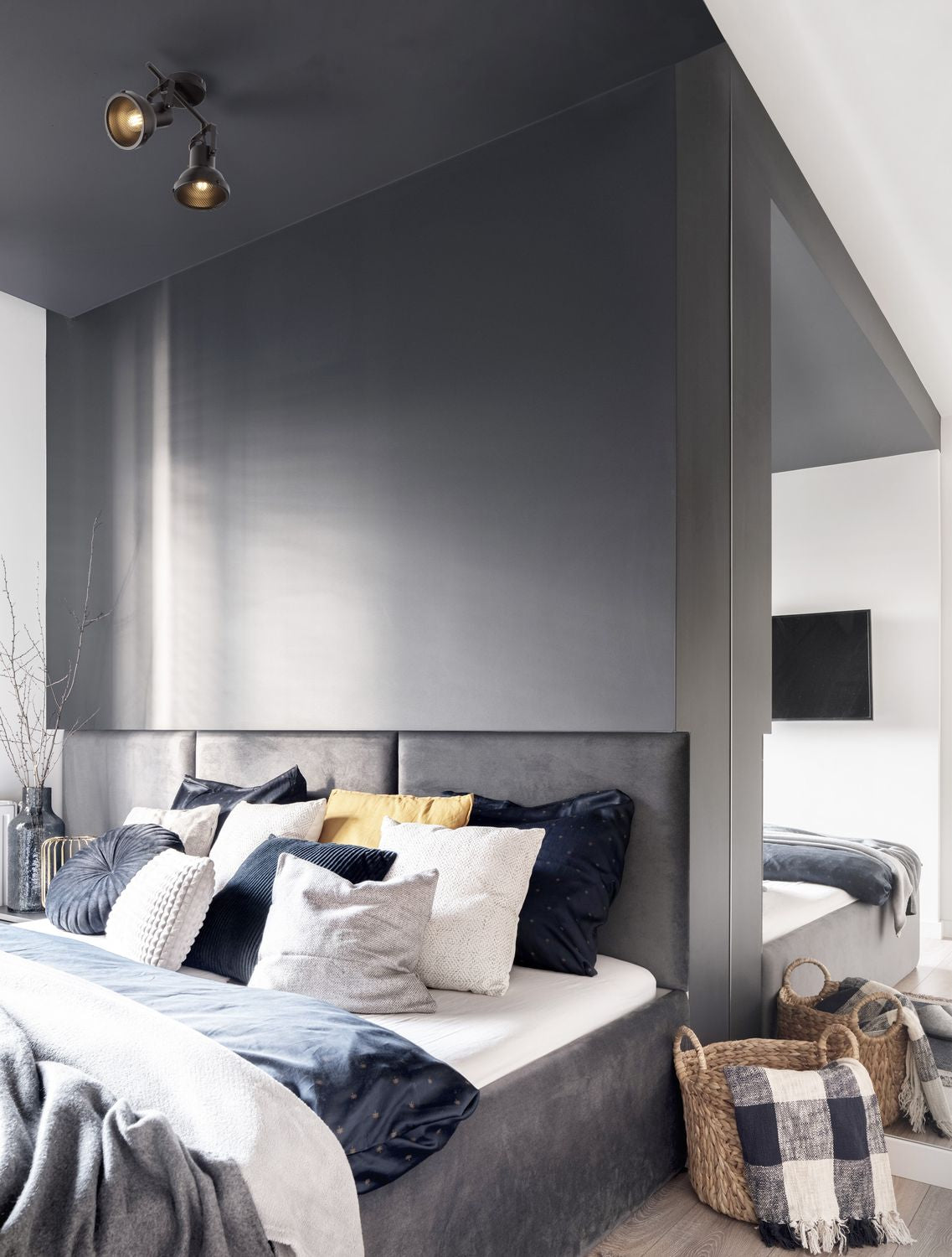 Plafonnier noir à deux spots orientables installé au-dessus d'un grand lit gris