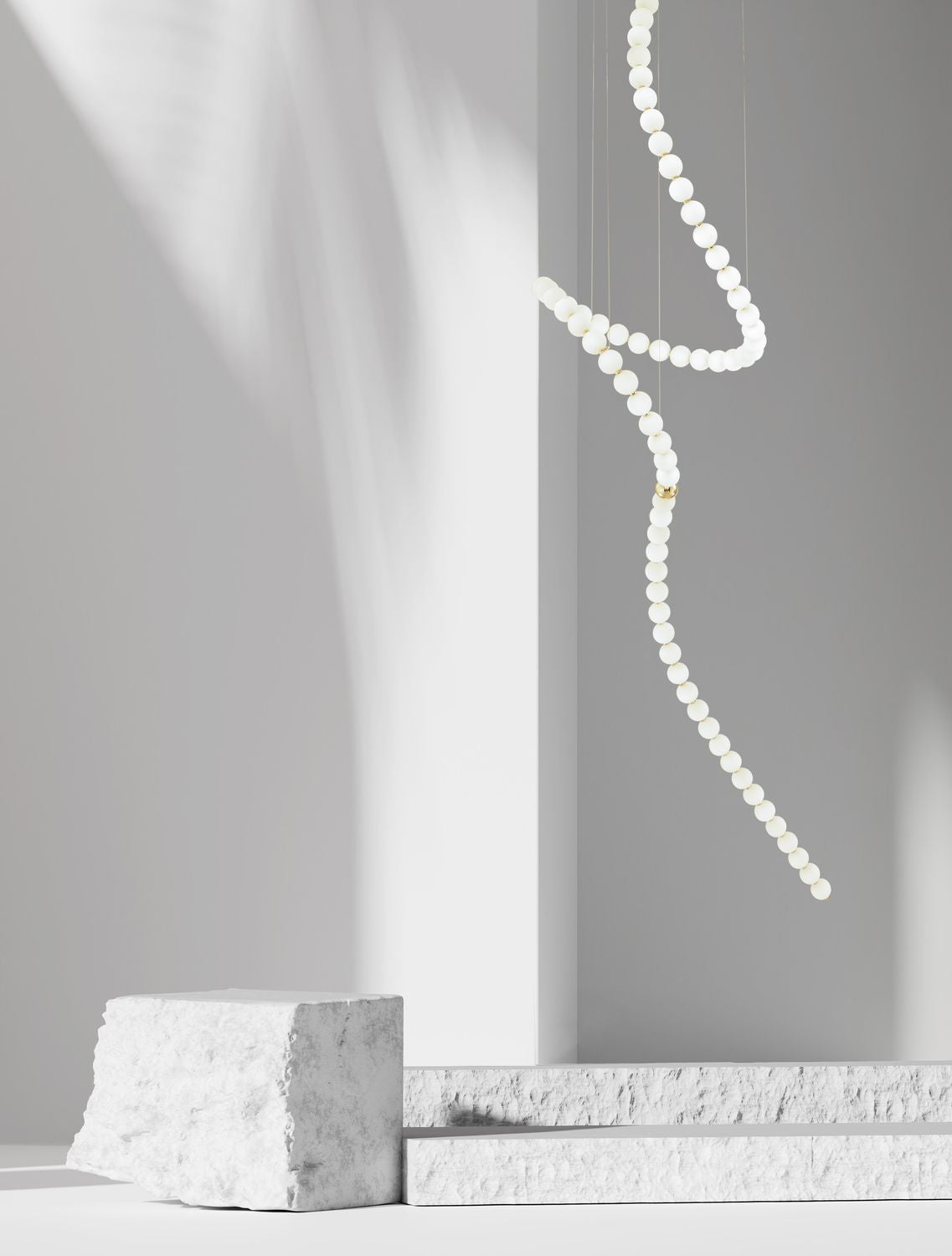 Suspension sculpturale en perles de verre blanc suspendue dans un décor minimal aux blocs de pierre