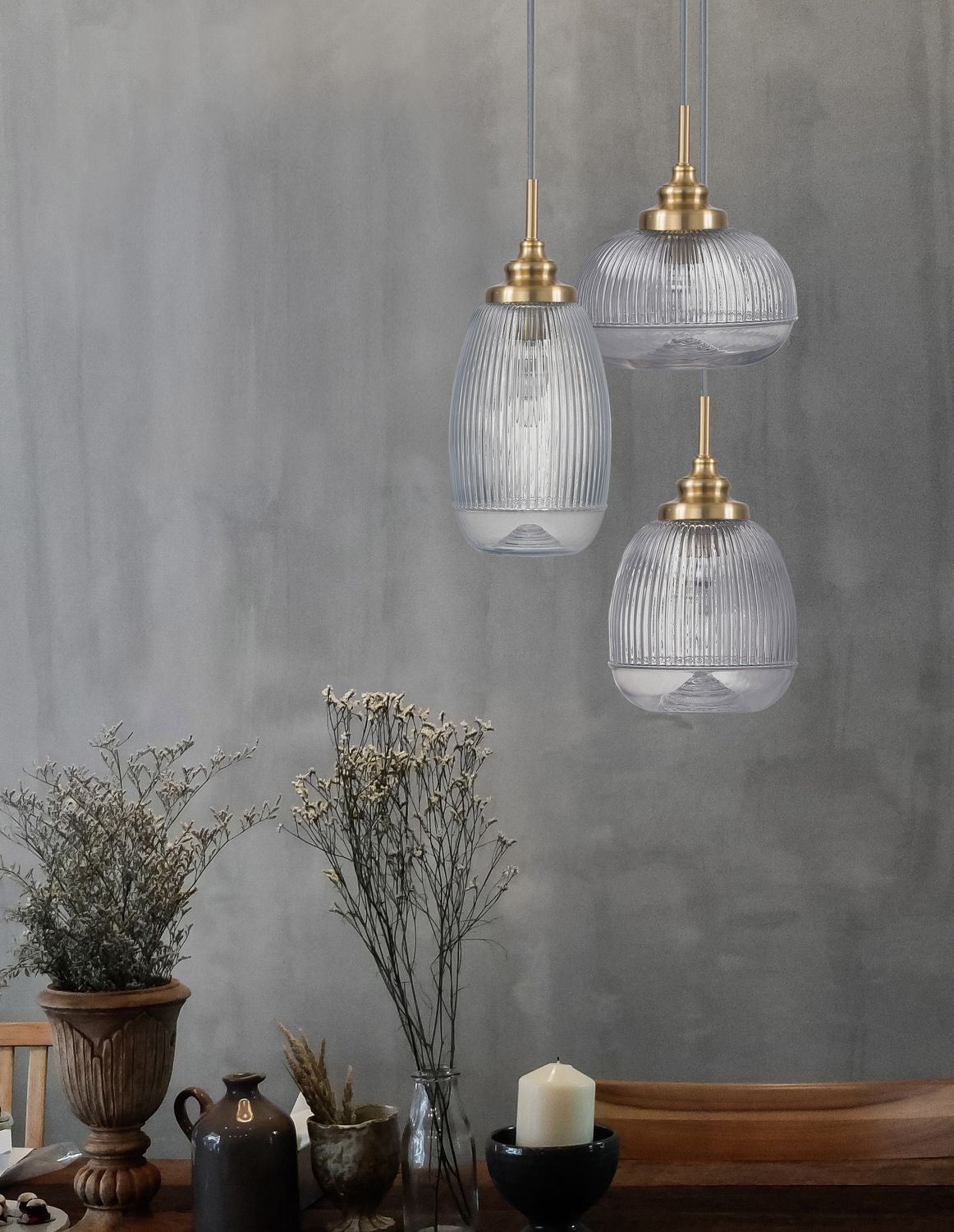 Mise en ambiance sur mur gris, suspensions dorées au-dessus de fleurs séchées
