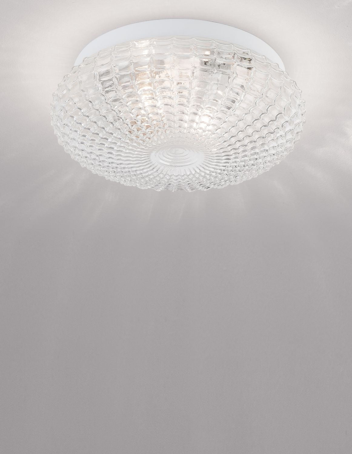 Plafonnier en verre transparent fixé au plafond blanc, lumière allumée en ambiance