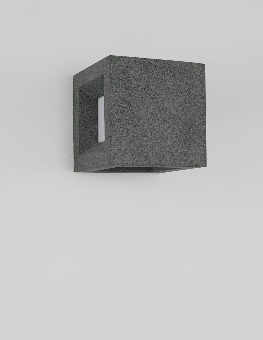Vue de trois quarts sur mur blanc, montrant le cube gris et sa fixation murale.