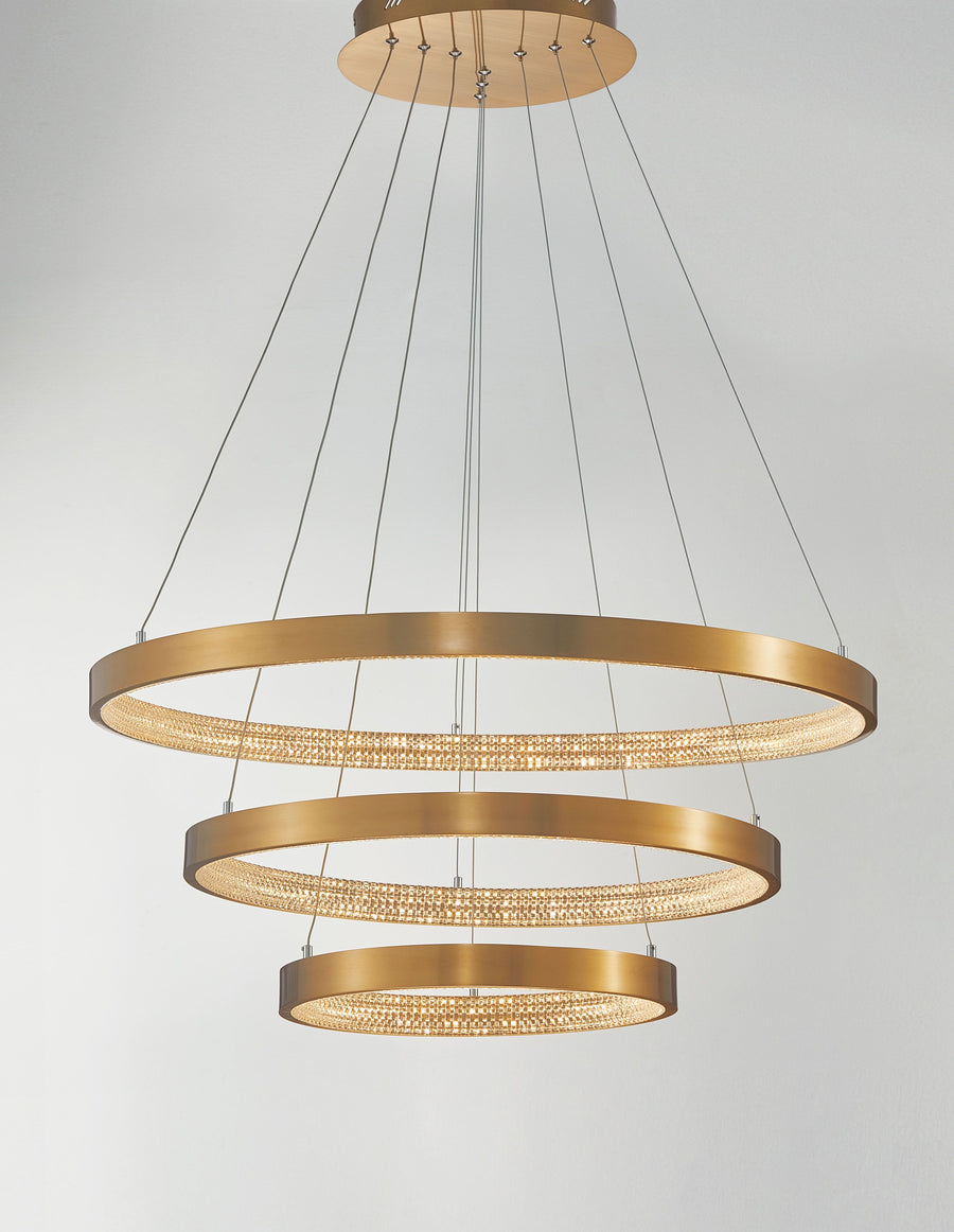 Vue de face du luminaire allumé, anneaux dorés diffusant une lumière chaude et scintillante
