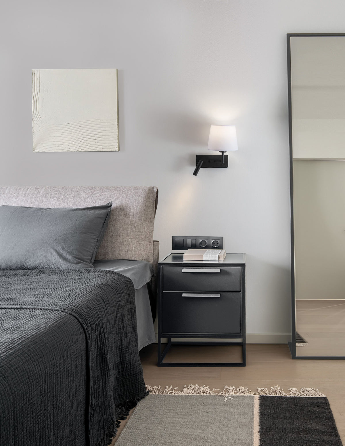 Vue en situation dans une chambre, applique allumée au-dessus de la table de nuit