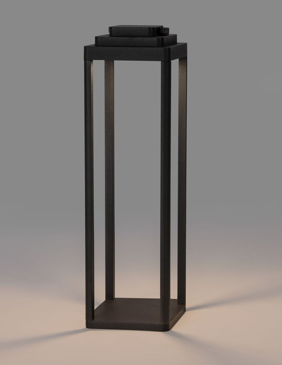 Lampadaire extérieur éclairé sur fond gris, diffusant une lumière chaude.