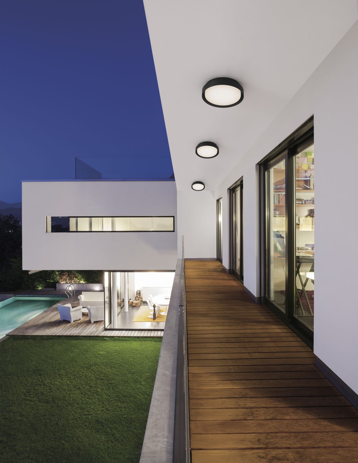 Vue nocturne d'une coursive extérieure avec trois luminaires ronds fixés au plafond