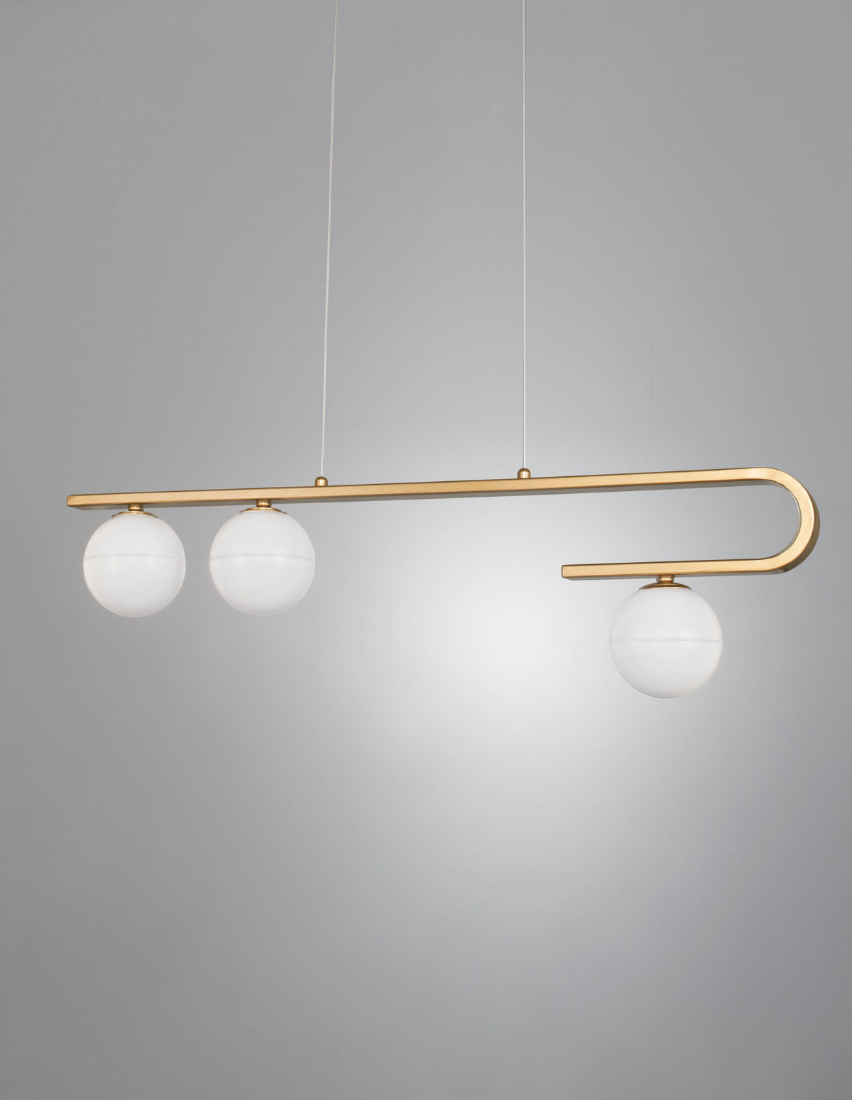 Détail du luminaire suspendu, bras doré recourbé et trois globes opalins